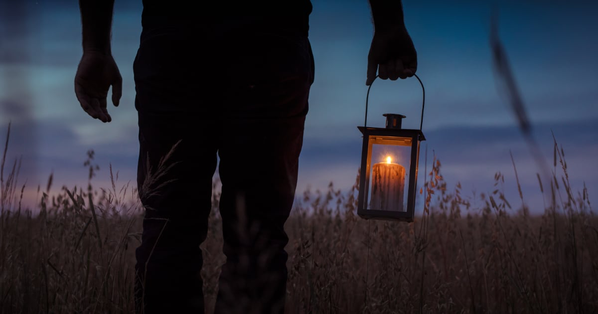 silhouette photo of man carrying candle lantern with lighted candle
